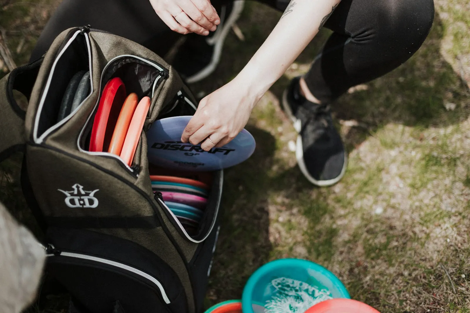 Open disc golf backpack on the course showing rows of putters and drivers as a player picks a disc