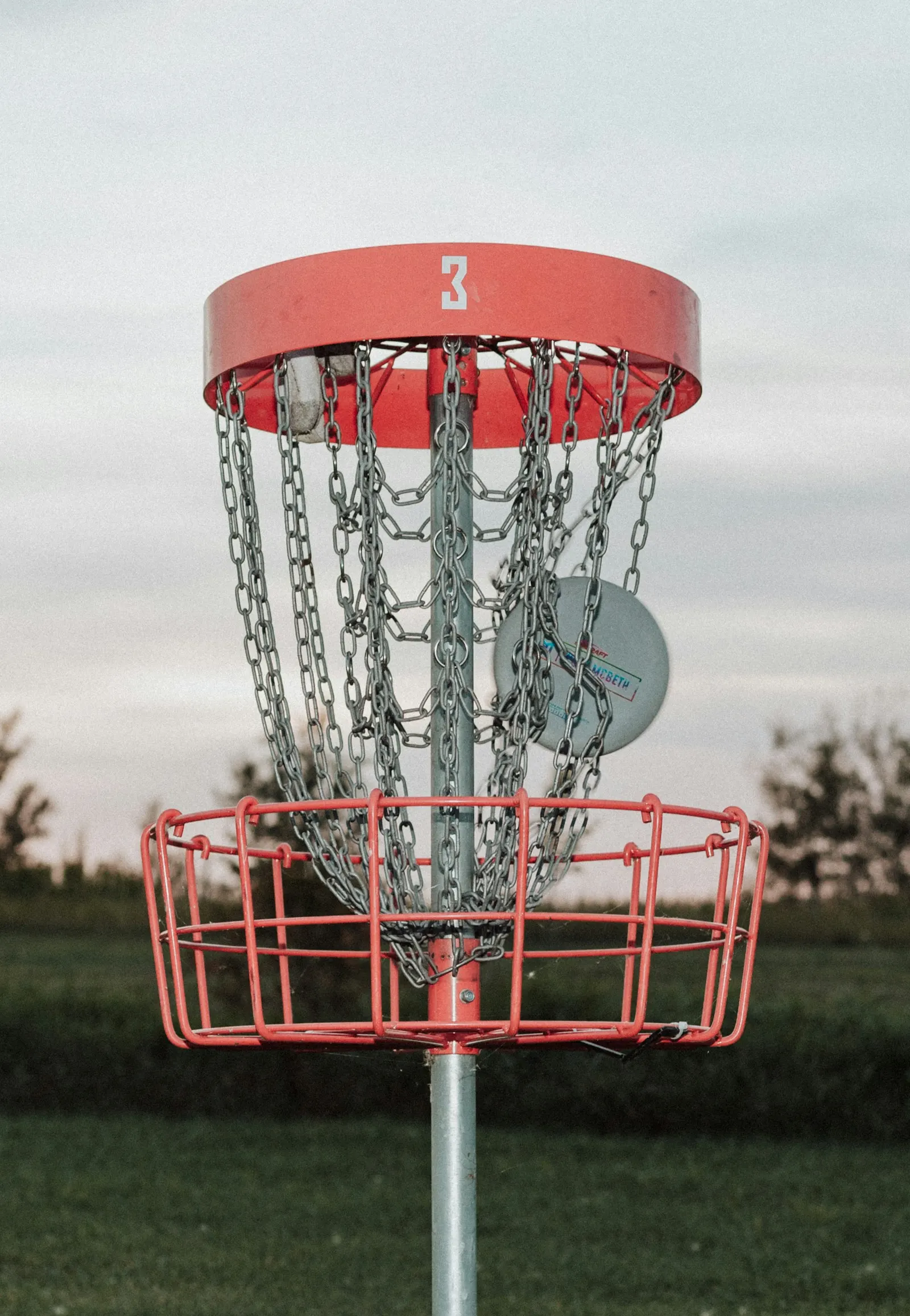 Red disc golf basket with silver chains catching a putter at golden hour