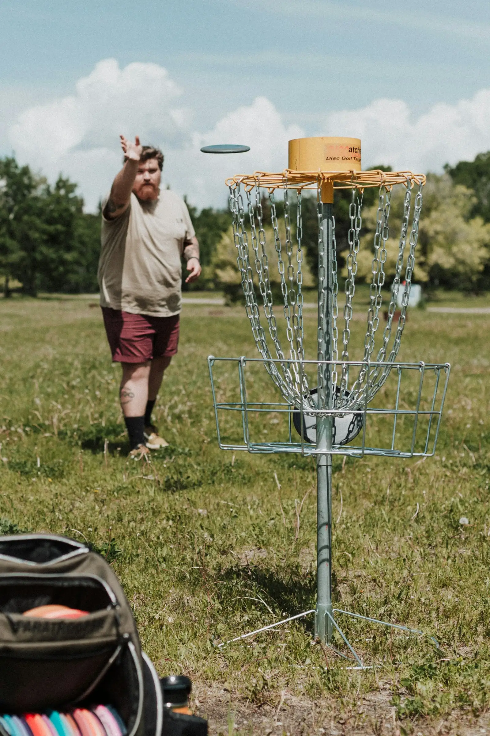 Player releasing a midrange disc toward a yellow-banded chain basket on a sunny course